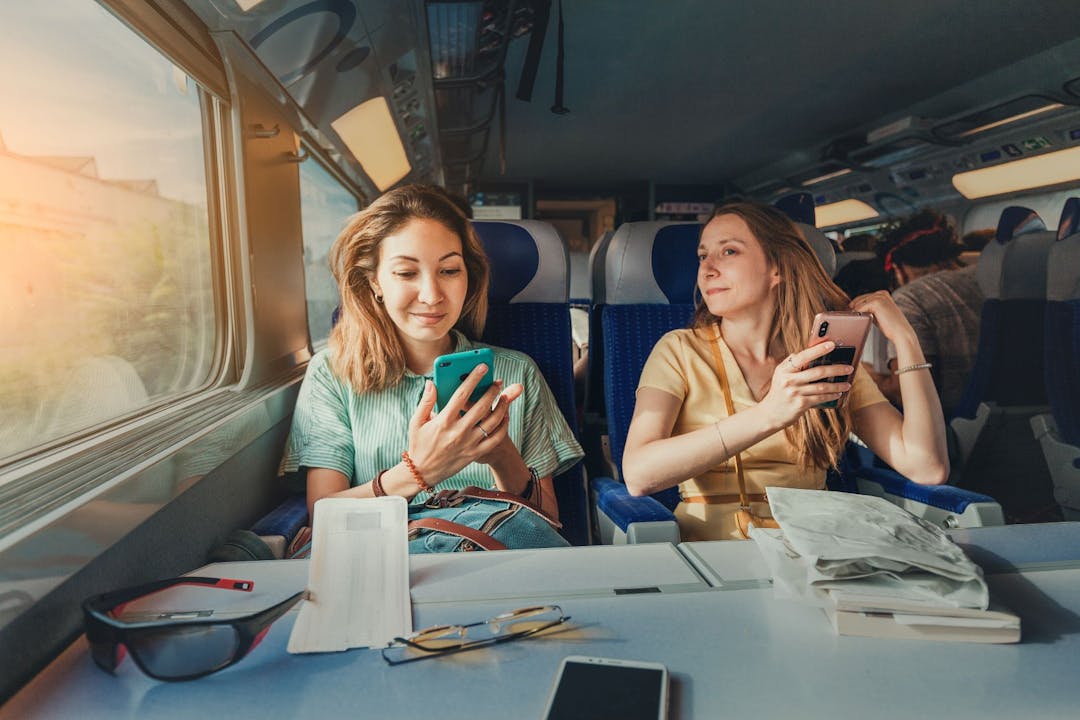 Zwei Frauen sitzen im Zug und schauen auf ihre Smartphones. 
