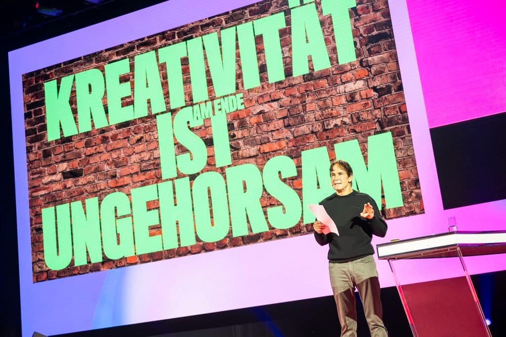 DMEXCO 2025 Keynote: Kreativität als Ungehorsam Vortragender auf der DMEXCO vor einem Bildschirm mit dem Zitat „Kreativität ist am Ende Ungehorsam“