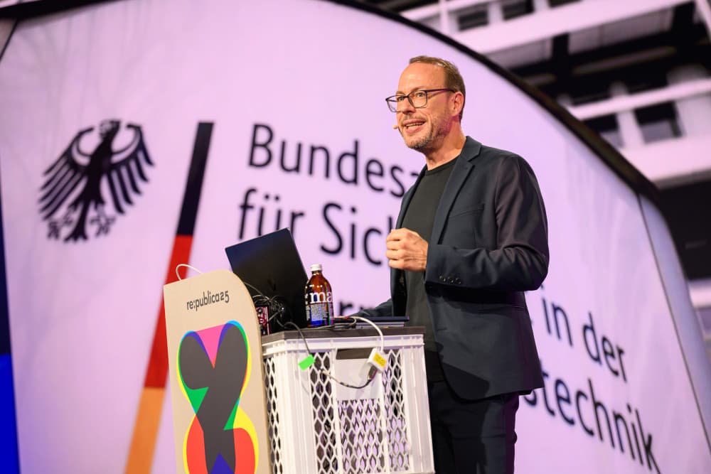 Markus Beckedahl auf der re:publica 25: „Datenschutz ist Brandschutz für die Demokratie“ Markus Beckedahl spricht auf der Bühne der re:publica 25 in Berlin. Hinter ihm ist eine große Projektion des Bundesadlers und des Schriftzugs „Bundesamt für Sicherheit in der Informationstechnik“ (BSI) zu. Am Pult der Konferenz steht sein Laptop neben einer Mate-Flasche.